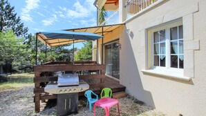 An outdoor patio with a barbecue grill, a covered seating area, and a window overlooking a garden. - 2 bedroom cozy home in Rousset les Vignes (Rousset les Vignes)
