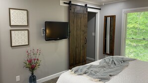 A bedroom with a bed, a TV mounted on the wall, a sliding door, and a window with a view of greenery. - Renovated!  Peaceful farm setting.  Close to TTU, town and Cummins Falls. (Cookeville)