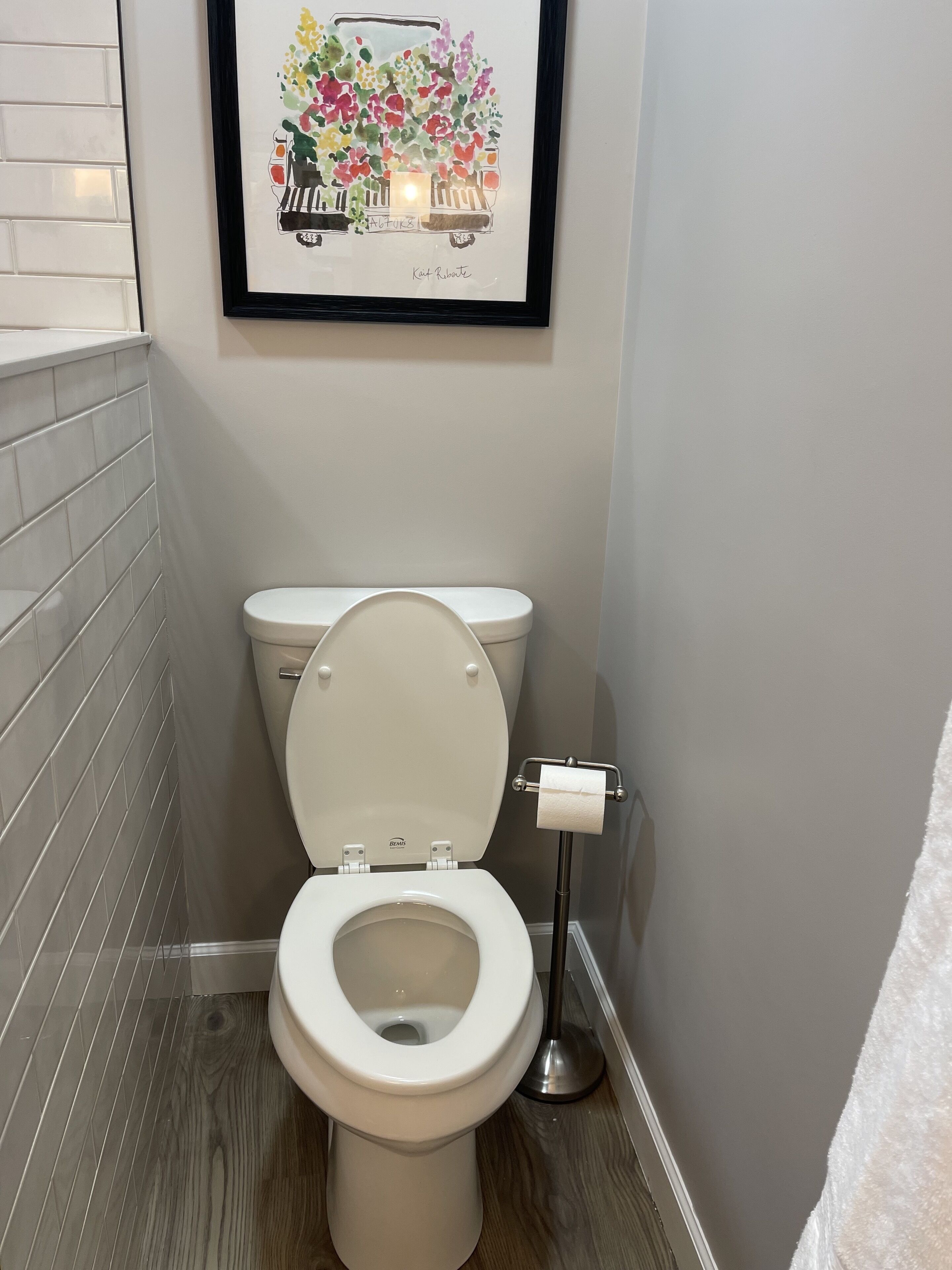A modern bathroom with a white toilet, a framed artwork above it, and a white towel rack.