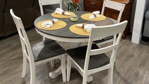 A dining area with a round table set for four, surrounded by white chairs. A cabinet with glass doors is visible in the background. - Renovated!  Peaceful farm setting.  Close to TTU, town and Cummins Falls. (Cookeville)