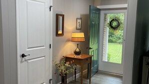 A hallway with wooden flooring, a white door, a table with a lamp and vase, and a green door with a wreath. - Renovated!  Peaceful farm setting.  Close to TTU, town and Cummins Falls. (Cookeville)