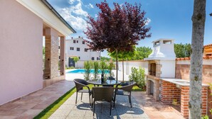 Eine Terrasse mit rundem Tisch und Stühlen, einem Grill und einem Pool im Hintergrund.