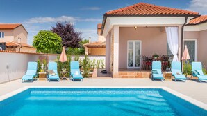 Ein Pool mit Liegestühlen, einer überdachten Terrasse und Blick auf die umliegenden Gebäude.