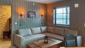Un salon chaleureux avec un canapé d’angle gris, une table basse en bois et une grande fenêtre donnant sur un paysage enneigé.