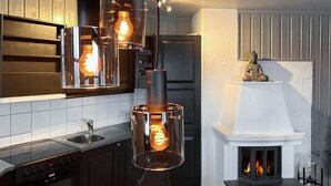 Une cuisine moderne dotée d’une cuisinière intégrée, d’une cheminée blanche et de luminaires suspendus avec des ampoules apparentes.