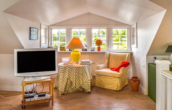 Une pièce confortable avec une télévision, une lampe, un fauteuil et une fenêtre donnant sur un paysage verdoyant.