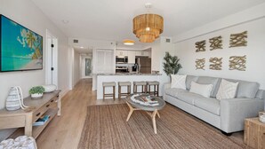 A modern living room with a grey sofa, a coffee table, and a dining area with bar stools.