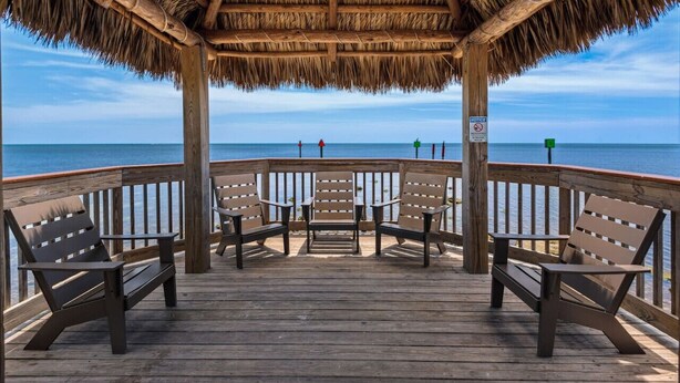 A wooden deck with thatched roof and benches overlooking the sea.