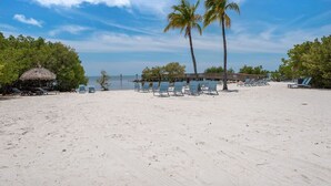 A beach with lounge chairs and a thatched-roof structure.