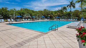 A swimming pool with lounge chairs and umbrellas, surrounded by palm trees and greenery.