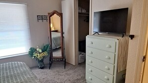 Un dormitorio con cama, cómoda, televisor, ventilador de techo y armario.