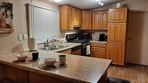 Una cocina con gabinetes de madera, encimera de granito, estufa, microondas y pileta.