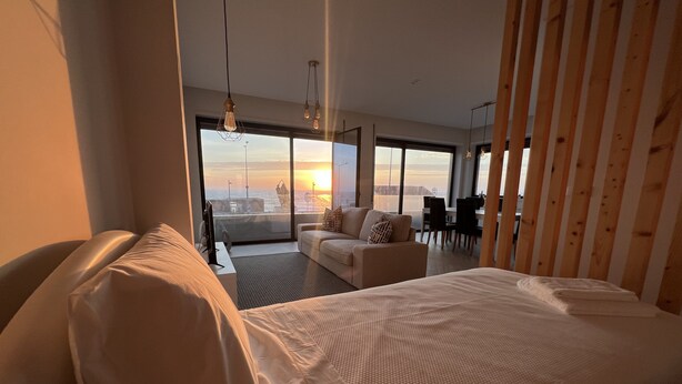 Habitació d'hotel moderna amb un llit gran, un sofà i zona menjador amb vistes al capvespre.