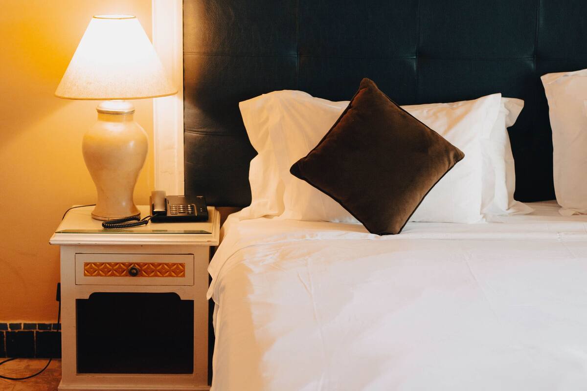 A hotel room with a bed, a nightstand with a lamp, and a telephone.