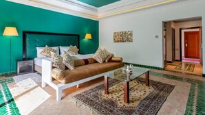 A hotel room with a teal accent wall, a sofa, a glass coffee table, and a patterned rug. - Palace Jena Hotel & Spa (Marrakech)