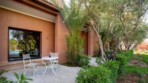 An outdoor seating area with two white metal chairs and a table, surrounded by gravel and greenery. - Palace Jena Hotel & Spa (Marrakech)