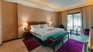 A hotel room with a large bed, two bedside lamps, a wooden bench, a purple rug, and a view of the outdoors. - Palace Jena Hotel & Spa (Marrakech)