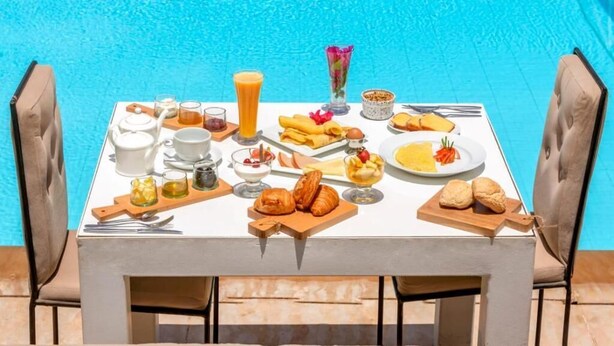 A breakfast table by a pool with various foods, drinks, and a vase of flowers. - Palace Jena Hotel & Spa (Marrakech)