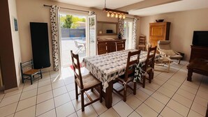 Un espace repas avec une table dressée pour six personnes, un coin cuisine et un coin salon avec un téléviseur et un meuble.