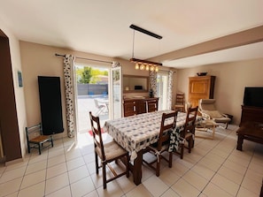 A dining area with a table set for six, a kitchen area, and a seating area with a TV and a cabinet.