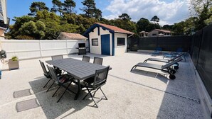 Une terrasse sur le toit avec une table et des chaises, un barbecue et un petit bâtiment bleu et blanc.