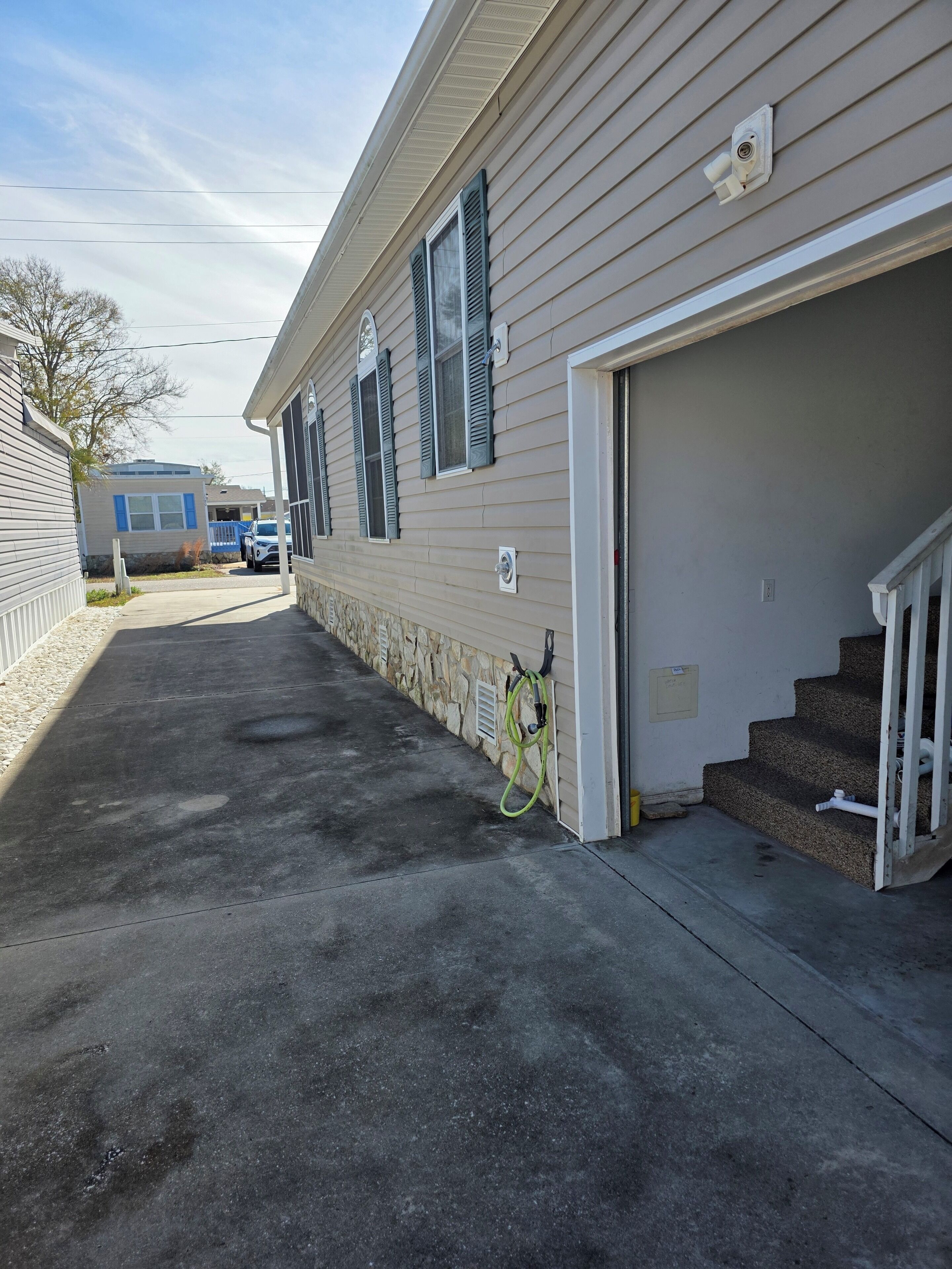 A single-story mobile home with a garage door, a stone foundation, and a concrete driveway.