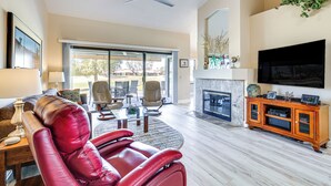 A spacious living room with a red leather sofa, a flat-screen TV mounted above a fireplace, and a ceiling fan.