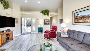A spacious living room with a flat-screen TV, leather armchair, and grey sofa.