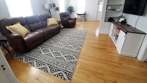A modern living room with a brown leather sofa, a patterned rug, and a wooden floor.