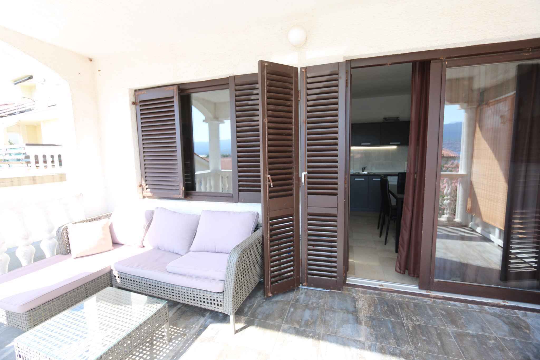 Un balcón con sofá de mimbre, una mesa de vidrio y una puerta corrediza con contraventanas, con vistas al interior.