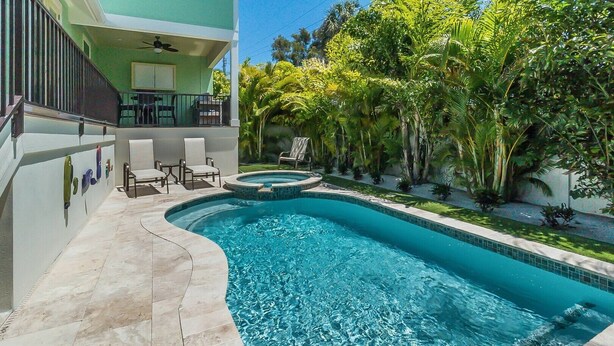 A swimming pool with a curved design, surrounded by a tiled deck and outdoor furniture. - Pineapple Cay: 2.5 Blocks to Beach! Pool & Spa by Anna Maria Life Vacation Rentals (Holmes Beach)
