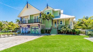 A two-story house with a balcony, a garage, and a well-maintained lawn. - Pineapple Cay: 2.5 Blocks to Beach! Pool & Spa by Anna Maria Life Vacation Rentals (Holmes Beach)