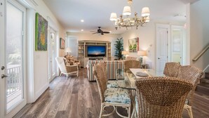 A spacious living room with a large TV, wicker furniture, and a chandelier. - Pineapple Cay: 2.5 Blocks to Beach! Pool & Spa by Anna Maria Life Vacation Rentals (Holmes Beach)