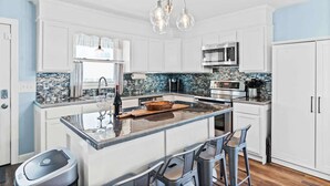 A modern kitchen with white cabinetry, a central island, bar stools, and a stainless steel refrigerator.