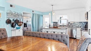 A modern kitchen with white cabinets, a central island, and a dining area with a wooden table and upholstered chairs.