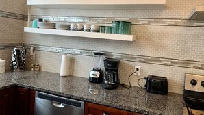 Een keuken met granieten aanrecht, een vaatwasser, een koffiezetapparaat, een broodrooster en een fornuis.