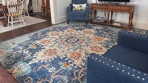 Een woonkamer met een groot, patroonrijk vloerkleed, een blauwe bank, een televisie en een plafondventilator.