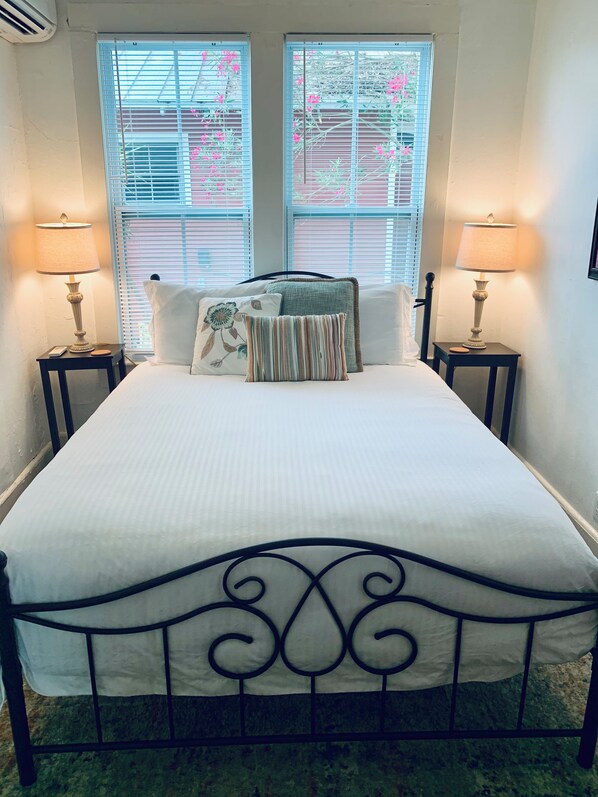 A bed with a metal frame, two bedside tables with lamps, and a window with blinds. - Downtown Lodge-Clean-Pet Friendly-Free Parking (St. Augustine)