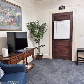 A room with a television, a plant, a blue sofa, and an exit sign.