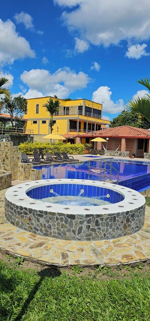 A swimming pool with a stone surround, a yellow building in the background, and a clear blue sky. - Hotel Bora Bora Campestre Los mangos (Quimbaya)