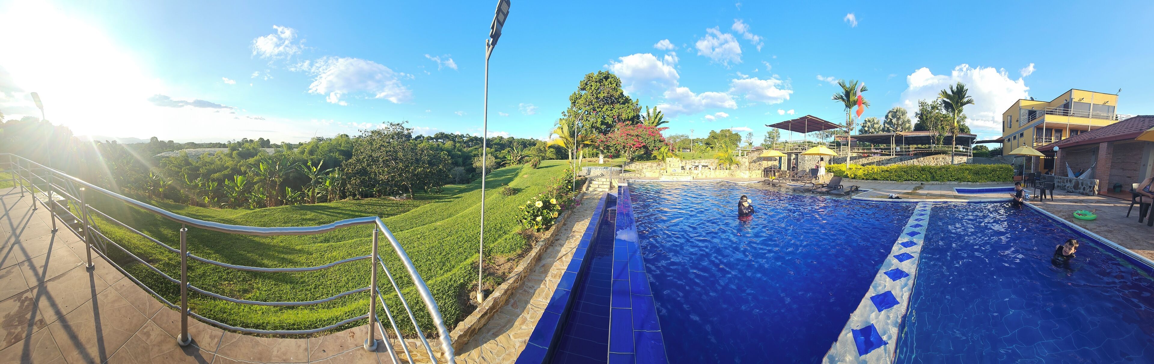 A swimming pool with a blue tiled edge, surrounded by a grassy area and a stone wall.