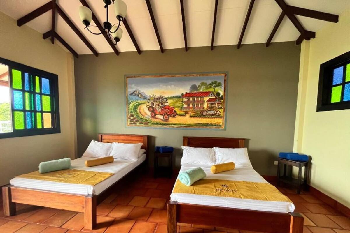 A room with two wooden beds, a painting on the wall, and a window with a view of greenery.