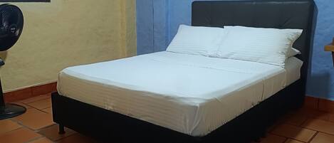 A bed with white bedding in a room with blue walls and a window with colorful glass panes.