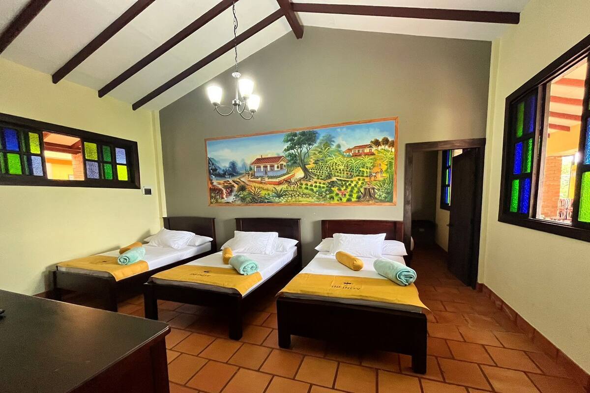A hotel room with two beds, a painting on the wall, and a table.