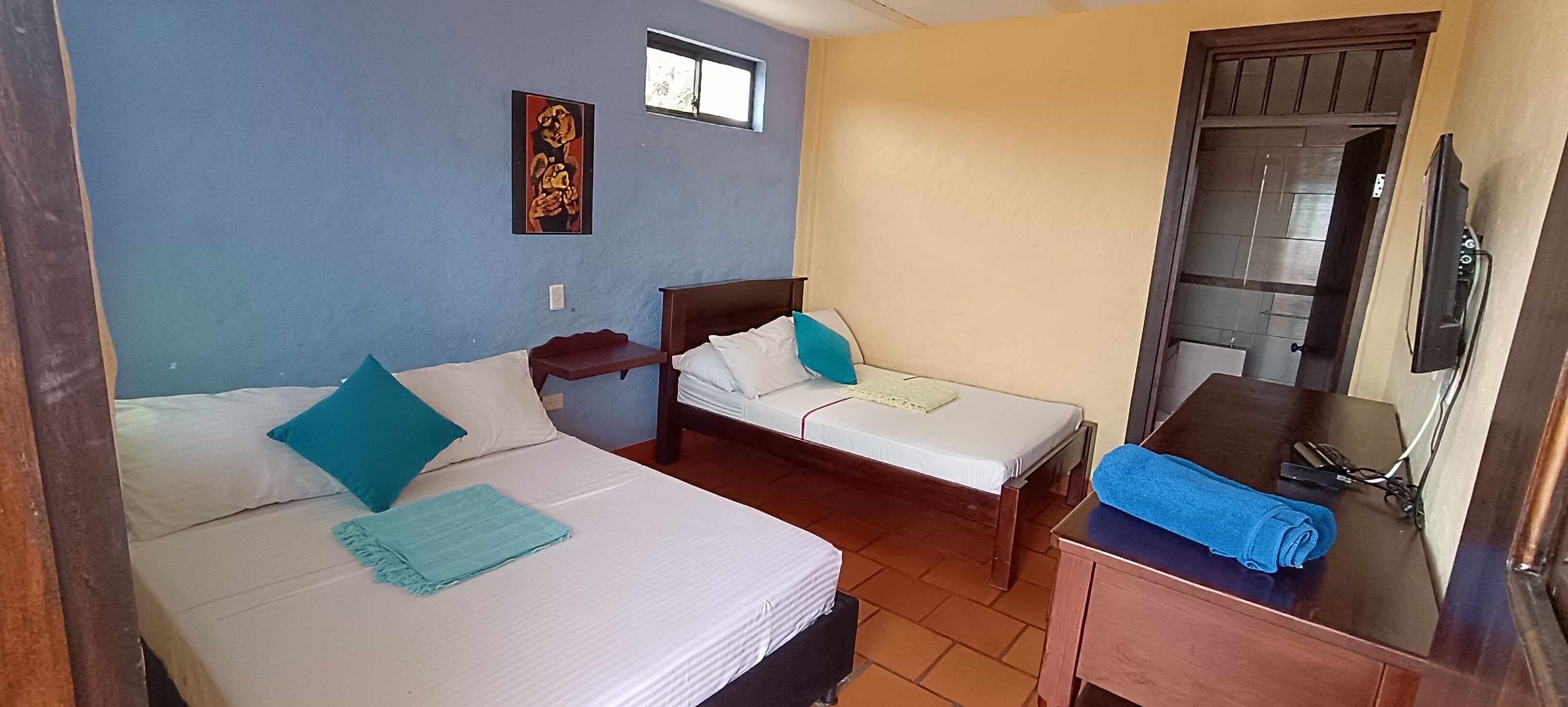 Habitación de hotel con dos camas, una mesita, televisión y ventana.