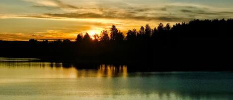 A calm lake at sunset with trees silhouetted against the sky.