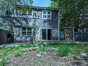 A two-story house with a front porch, a garage, and a fenced yard with plants and rocks.