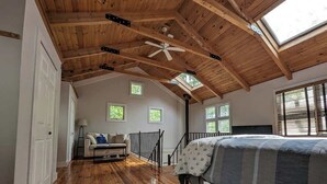 Quarto com teto de madeira, cama, janela e escada.