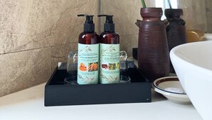 A bathroom with a large plant, two bottles of shampoo, and a vase on the counter. - Sea Sand 2 Hotel (Da Nang)