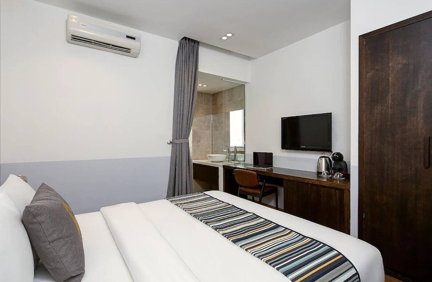 Quarto de hotel com cama, escrivaninha, televisão e ar condicionado.